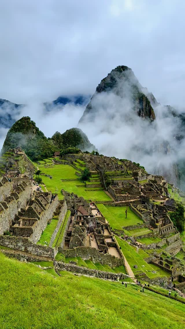 Ancient stone ruins of Machu Picchu nestled among green mountains and white clouds.