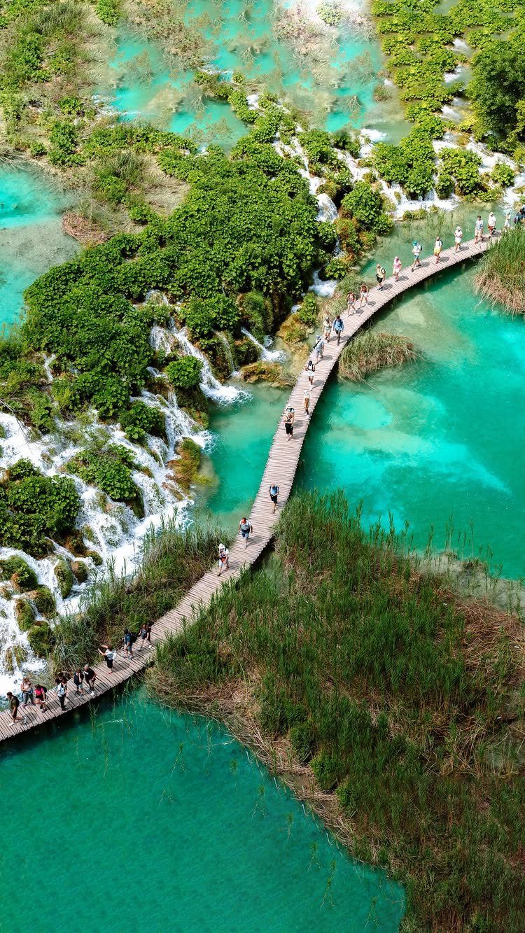 Wooden boardwalk curving through turquoise lakes and cascading waterfalls in a lush park.