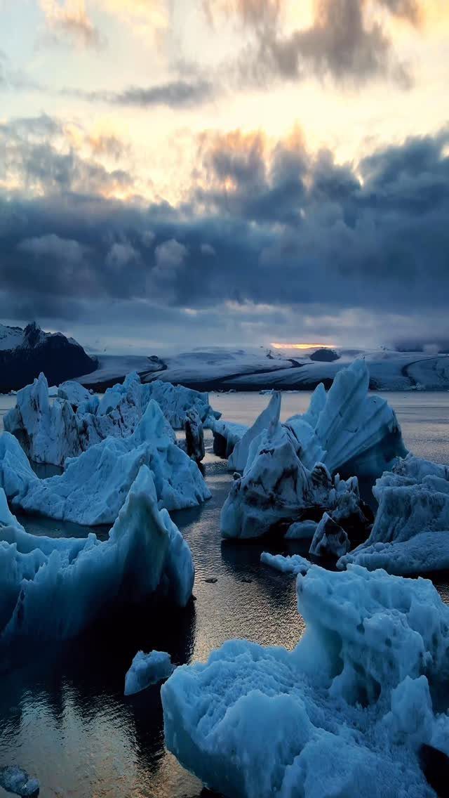 Jagged blue icebergs floating in a glacial lagoon under a cloudy sunset sky.