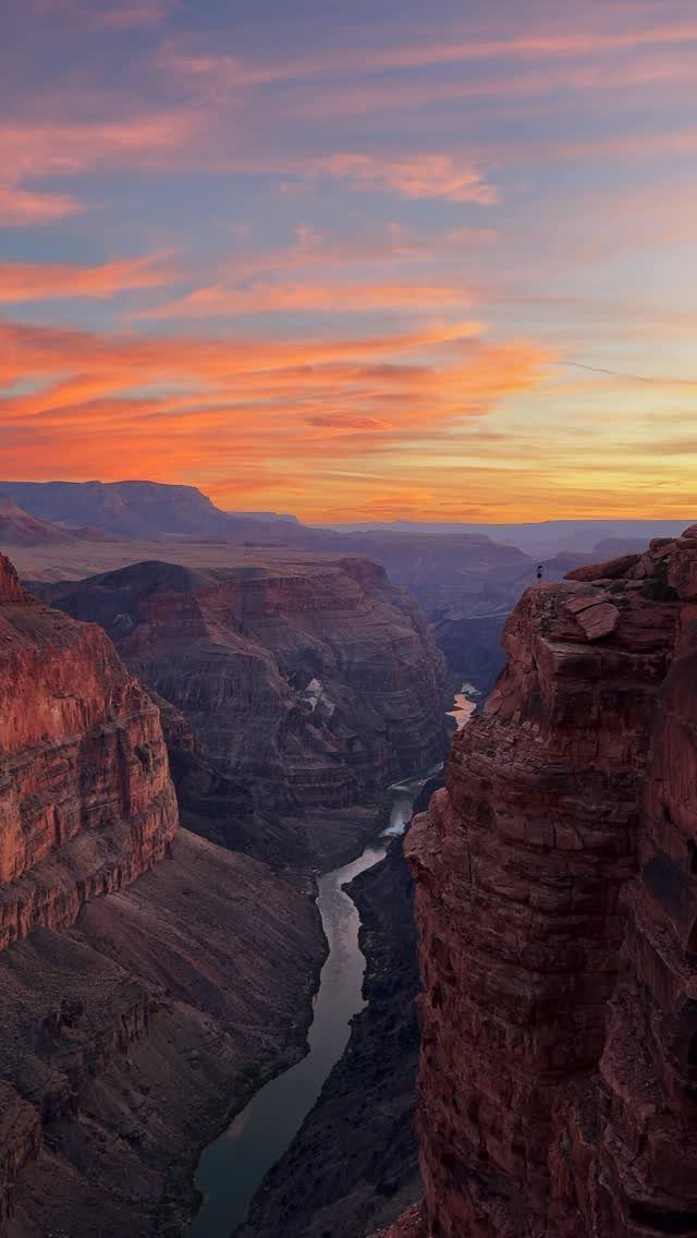 Deep red rock canyon with a winding river under a sunset sky.