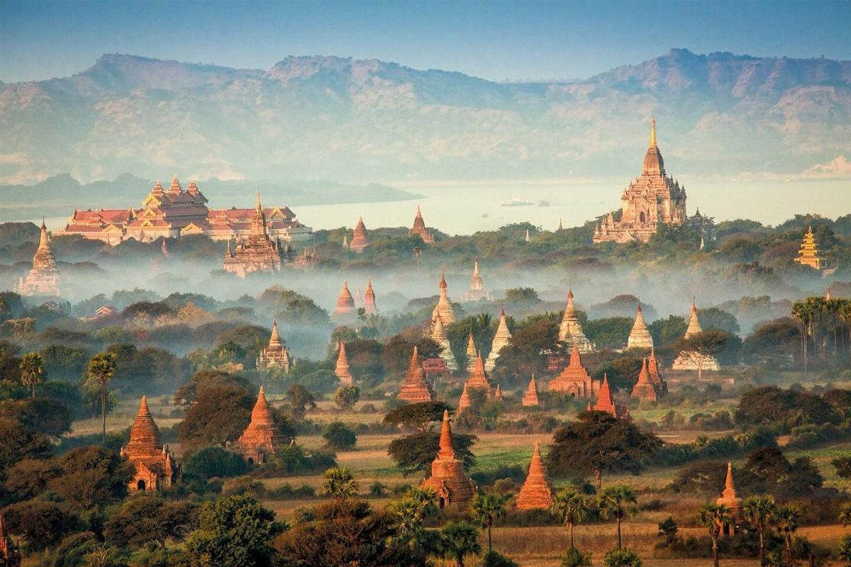 Numerous ancient brick pagodas scattered across a misty plain with distant blue mountains.