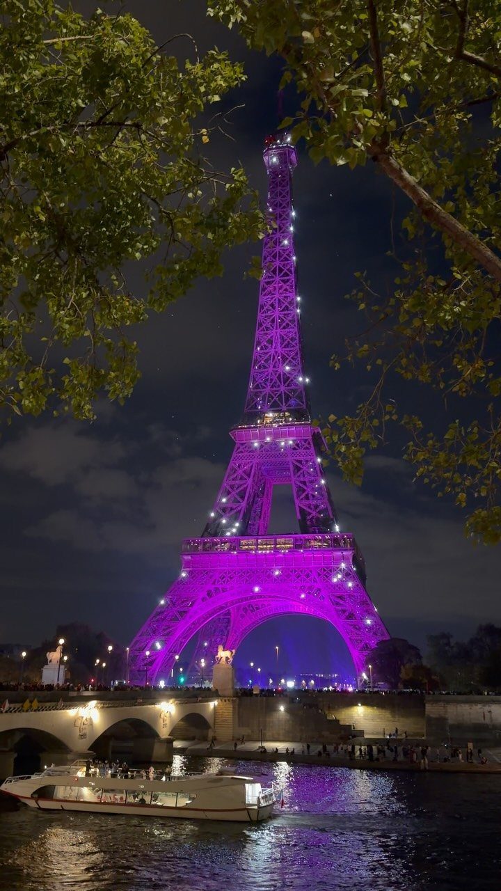 Eiffel Tower glowing purple at night with a boat on the Seine river