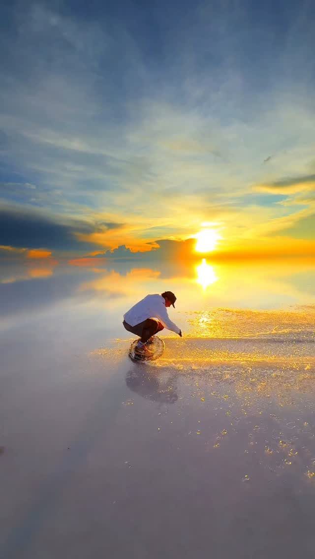 Person riding a bicycle across a reflective salt flat during a golden sunset.