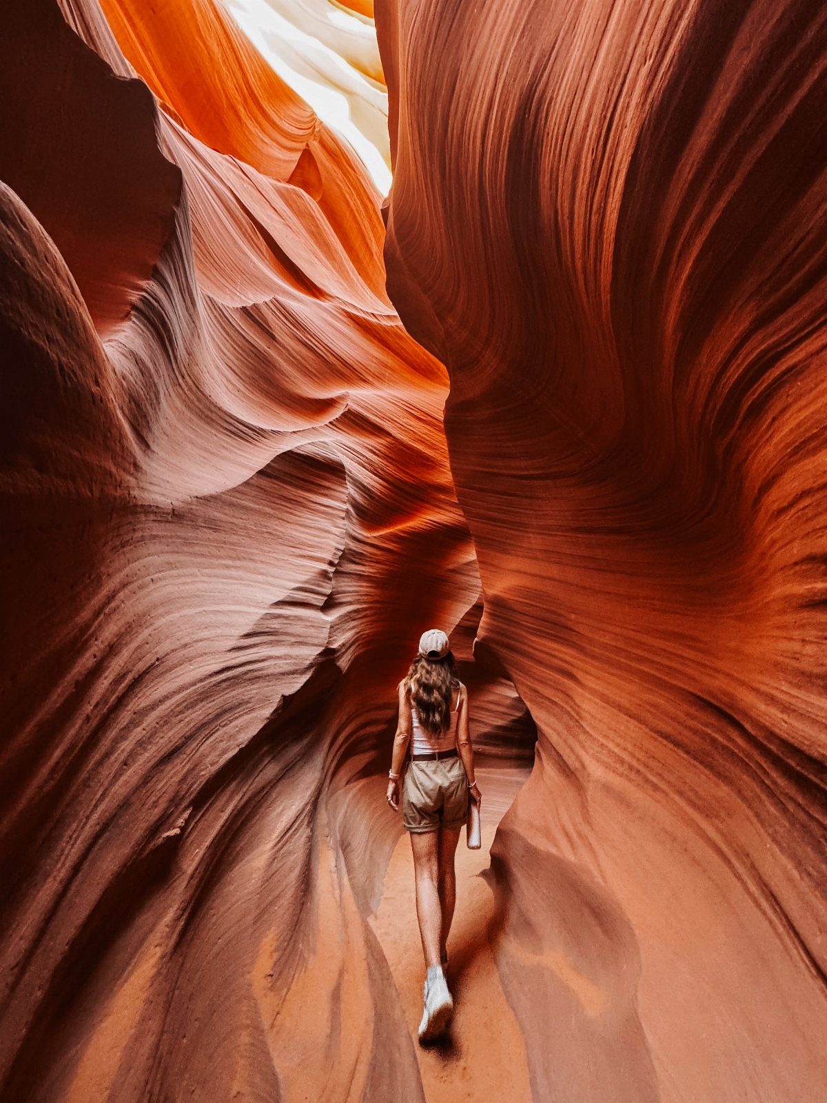 Woman walking through the flowing orange sandstone walls of Antelope Canyon slot canyon.