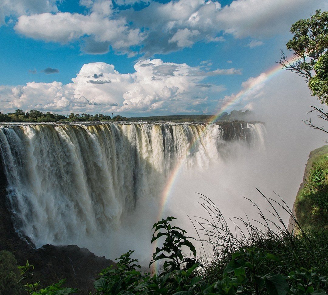 Wide waterfall with cascading white water and a rainbow under a cloudy sky