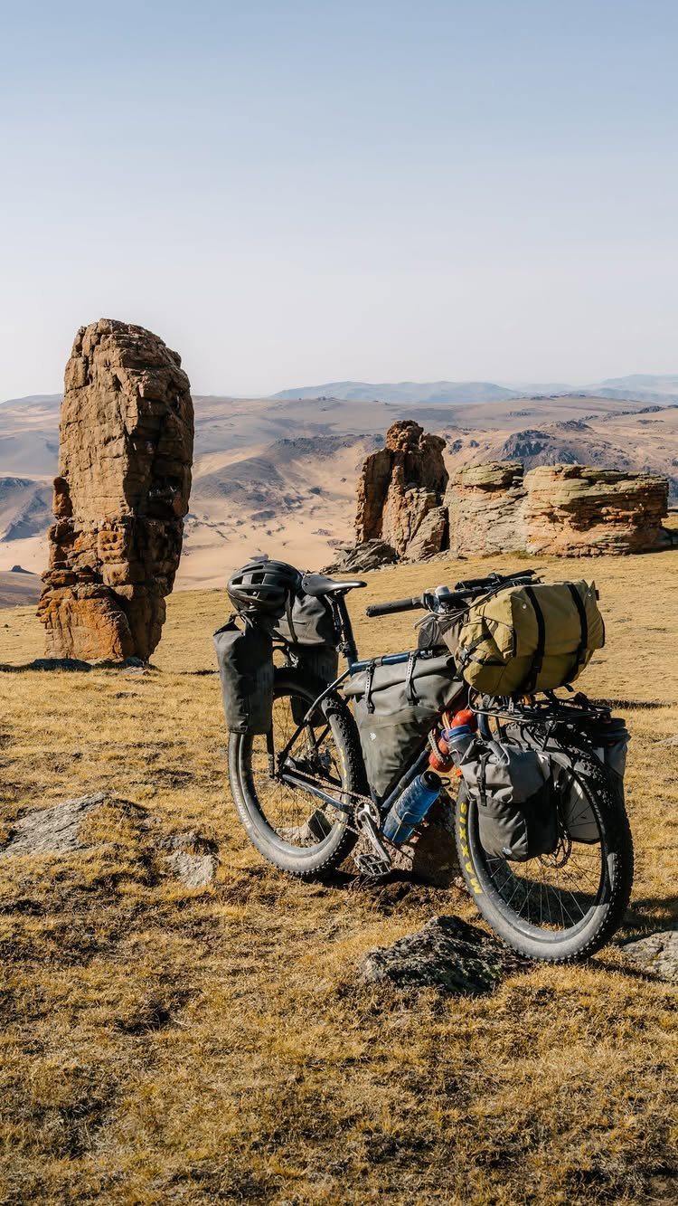 16 Adventurous Places to Travel, From Utah to Mongolia 7 Bikepacking bicycle with gear parked on a grassy plain with jagged rock formations.