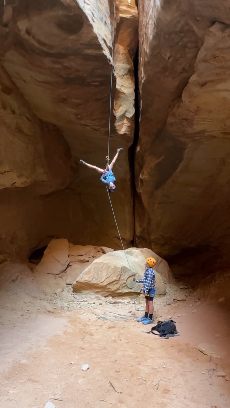 16 Adventurous Places to Travel, From Utah to Mongolia 1 Person rappelling down a rope in a narrow orange sandstone slot canyon.