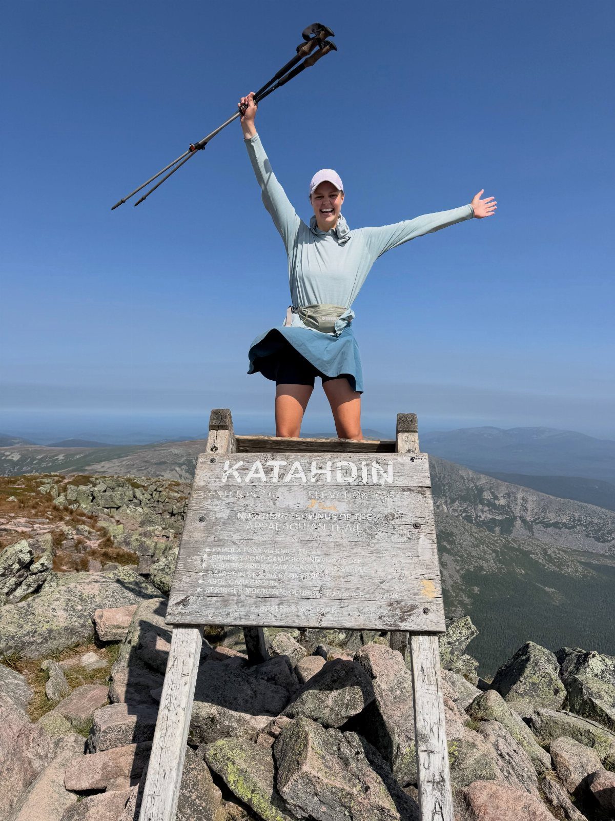 16 Adventurous Places to Travel, From Utah to Mongolia 4 Woman celebrating on top of the Katahdin sign at a rocky mountain summit