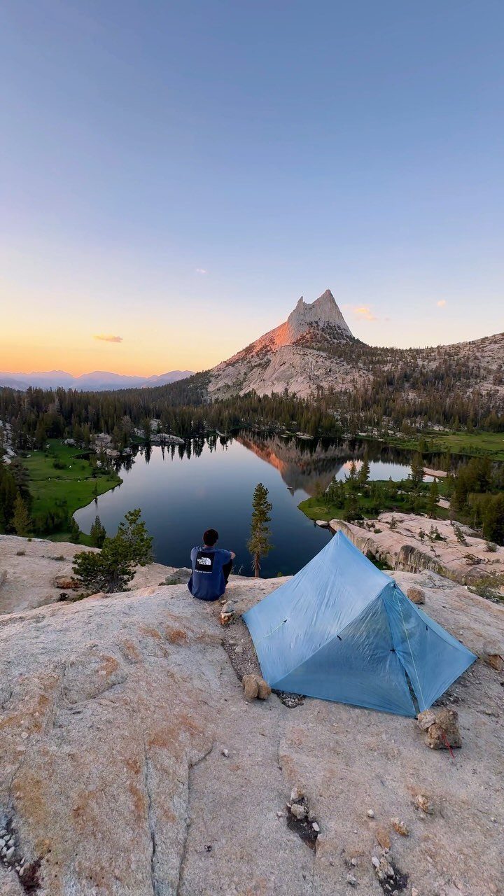 16 Adventurous Places to Travel, From Utah to Mongolia 2 Person sitting by a blue tent overlooking a mountain lake at sunset