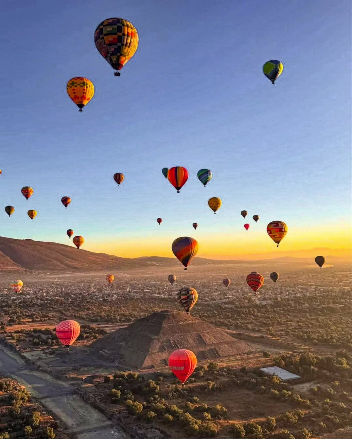 16 Adventurous Places to Travel, From Utah to Mongolia 14 Colorful hot air balloons floating over an ancient stone pyramid at sunrise.