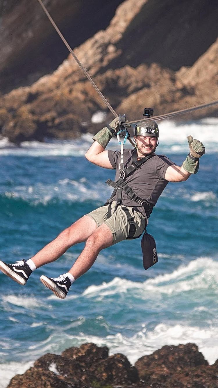 16 Adventurous Places to Travel, From Utah to Mongolia 8 Man ziplining over a blue ocean with rocky cliffs and white waves.