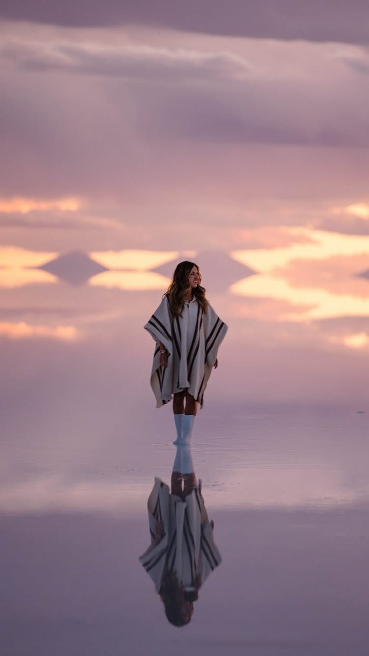 16 Adventurous Places to Travel, From Utah to Mongolia 15 Woman in a poncho standing on a reflective salt flat under a sunset sky.