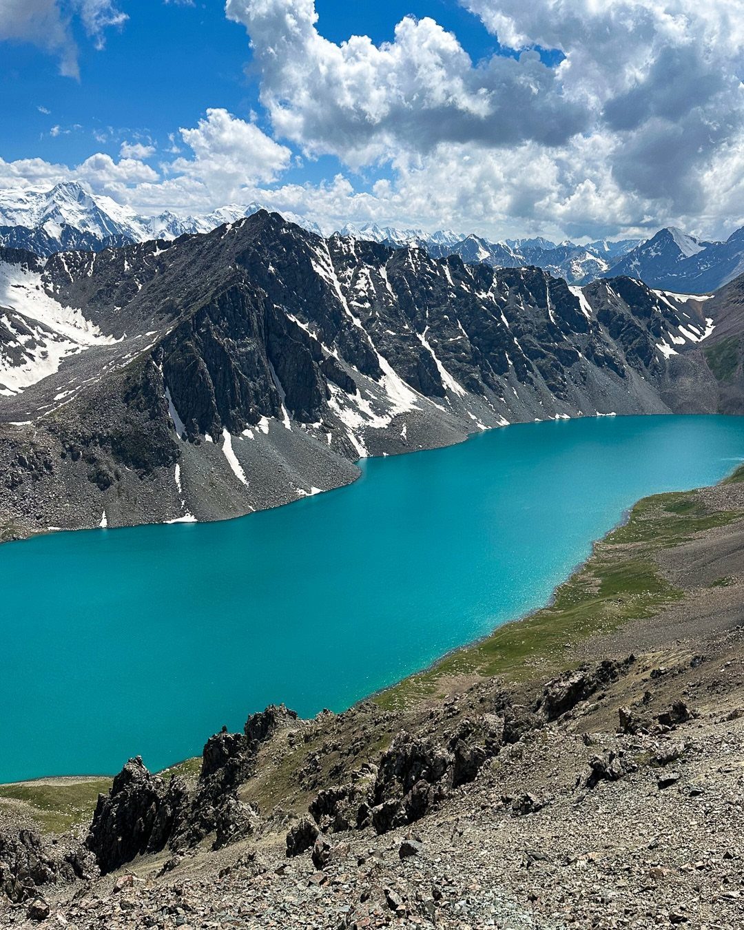 16 Adventurous Places to Travel, From Utah to Mongolia 11 Turquoise alpine lake surrounded by rugged snow-capped mountains under a cloudy blue sky.