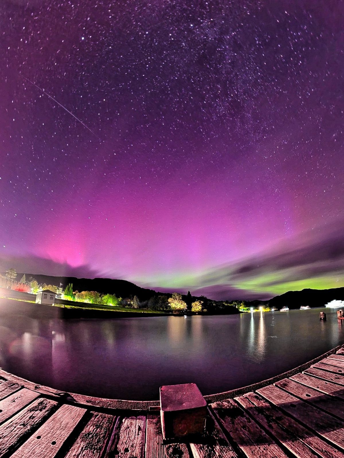 Purple and green aurora borealis over a lake with a wooden pier foreground.