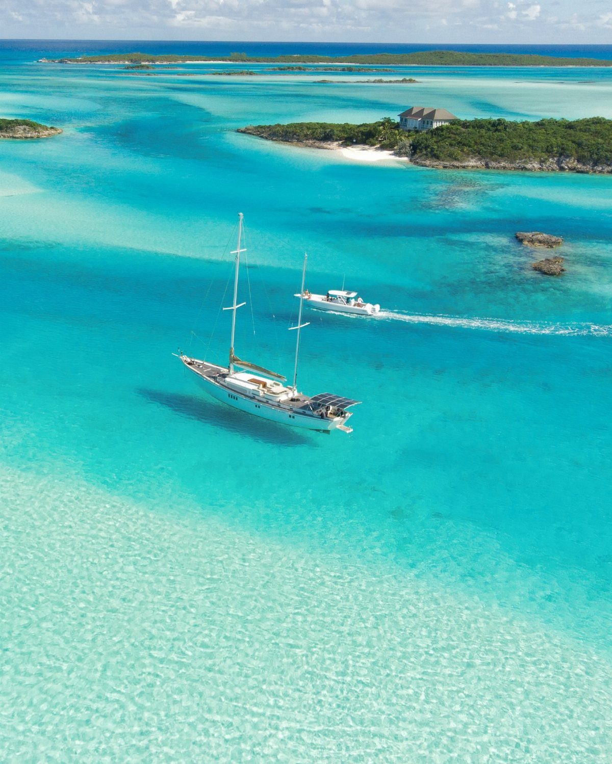 Beach Places to Travel: 13 Ideas for Your Next Trip 9 White sailboat and motorboat floating in turquoise tropical waters near sandy islands.