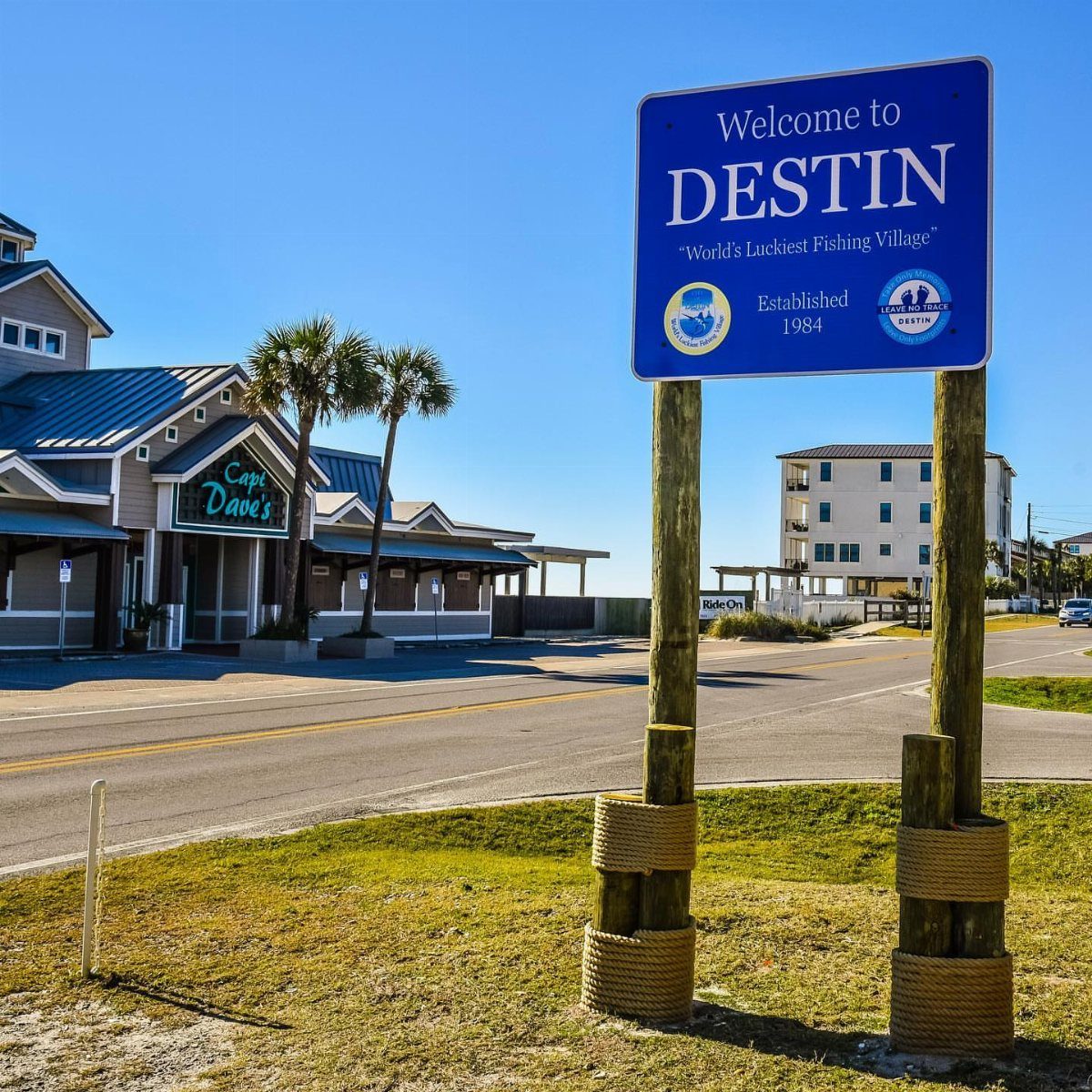 Beach Places to Travel: 13 Ideas for Your Next Trip 3 Welcome to Destin sign on wooden posts with palm trees and buildings behind.