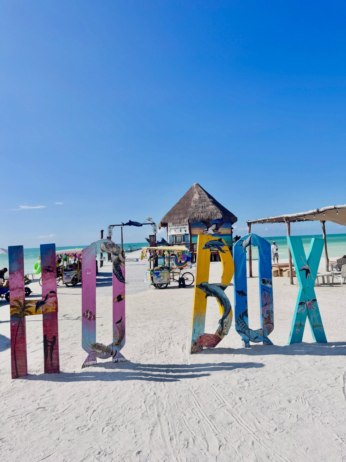 Beach Places to Travel: 13 Ideas for Your Next Trip 1 Colorful HOLBOX letters on a white sandy beach with a thatched hut background.
