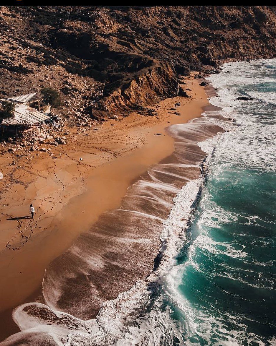Beach Places to Travel: 13 Ideas for Your Next Trip 6 Reddish-orange sand beach with turquoise ocean waves and steep brown rocky cliffs.