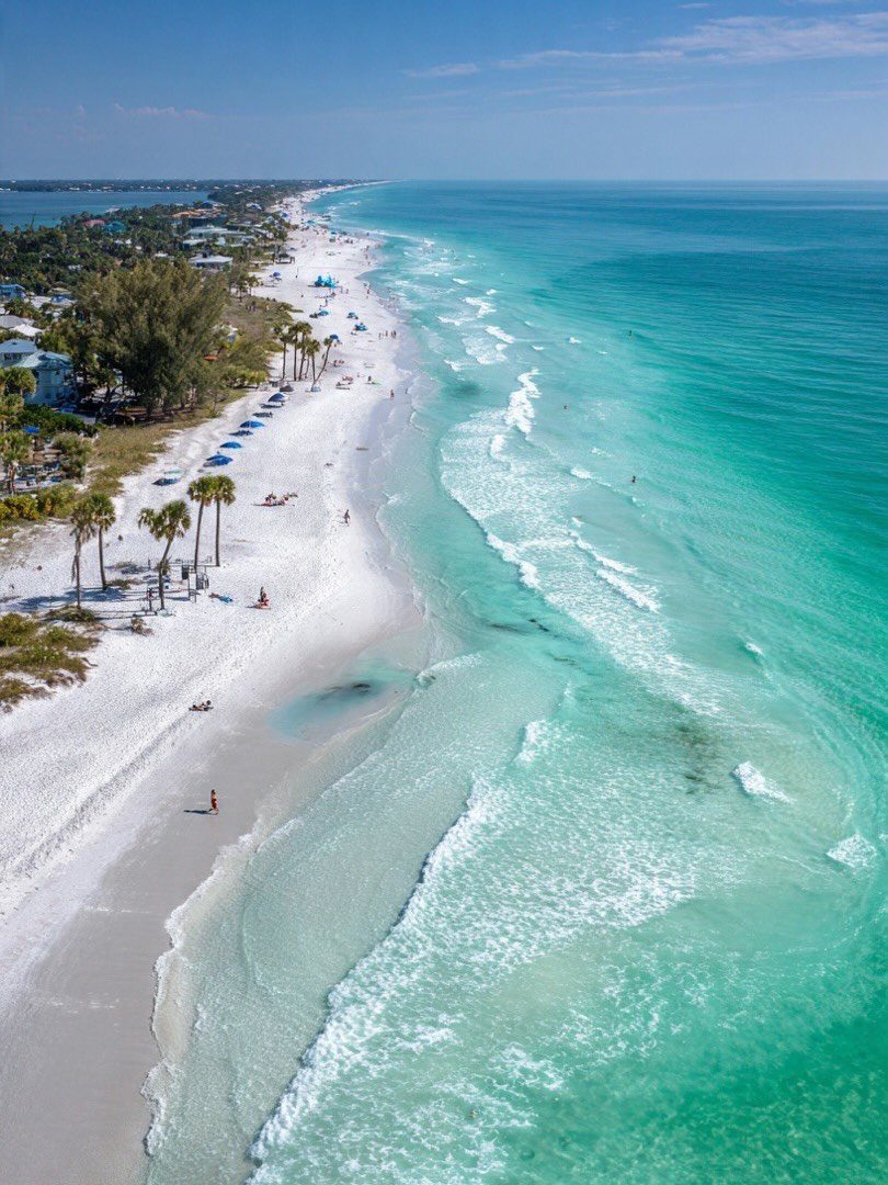 Beach Places to Travel: 13 Ideas for Your Next Trip 2 White sandy beach and turquoise ocean water with palm trees and coastal homes.