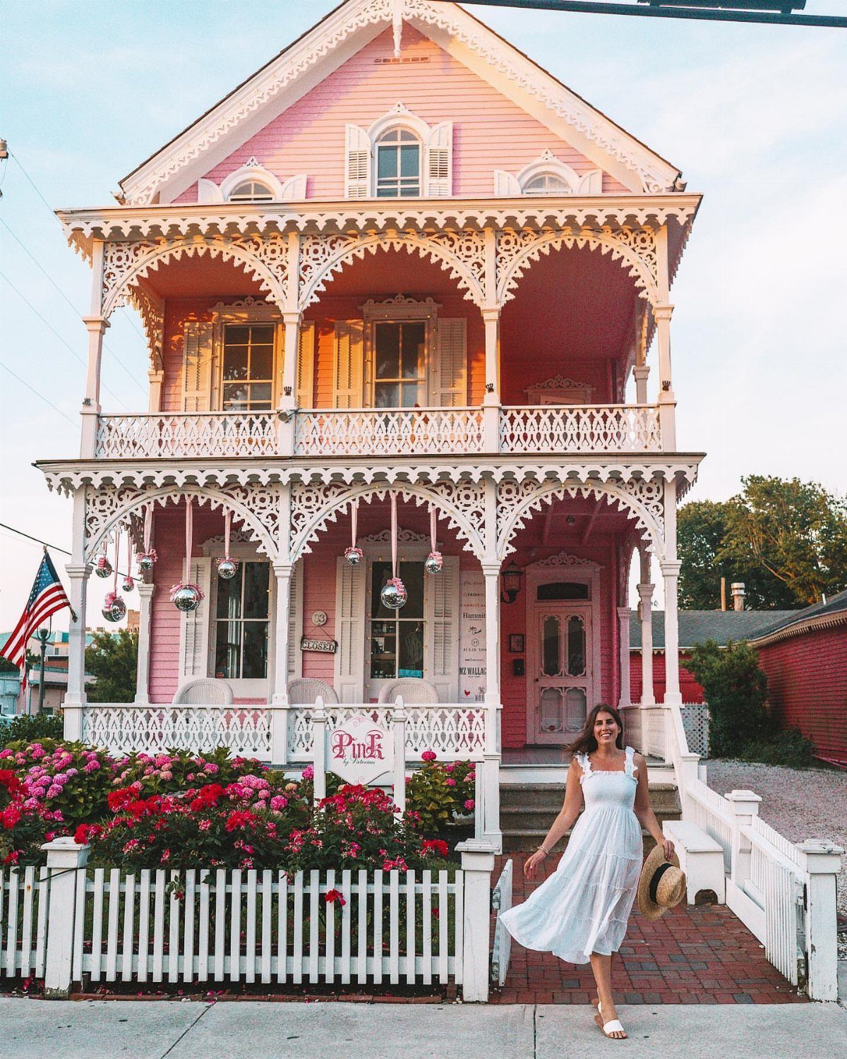 6 Beach Places to Visit, From Cape May to the Kona Coast 5 Woman in white dress standing before a pink Victorian house with ornate white trim.