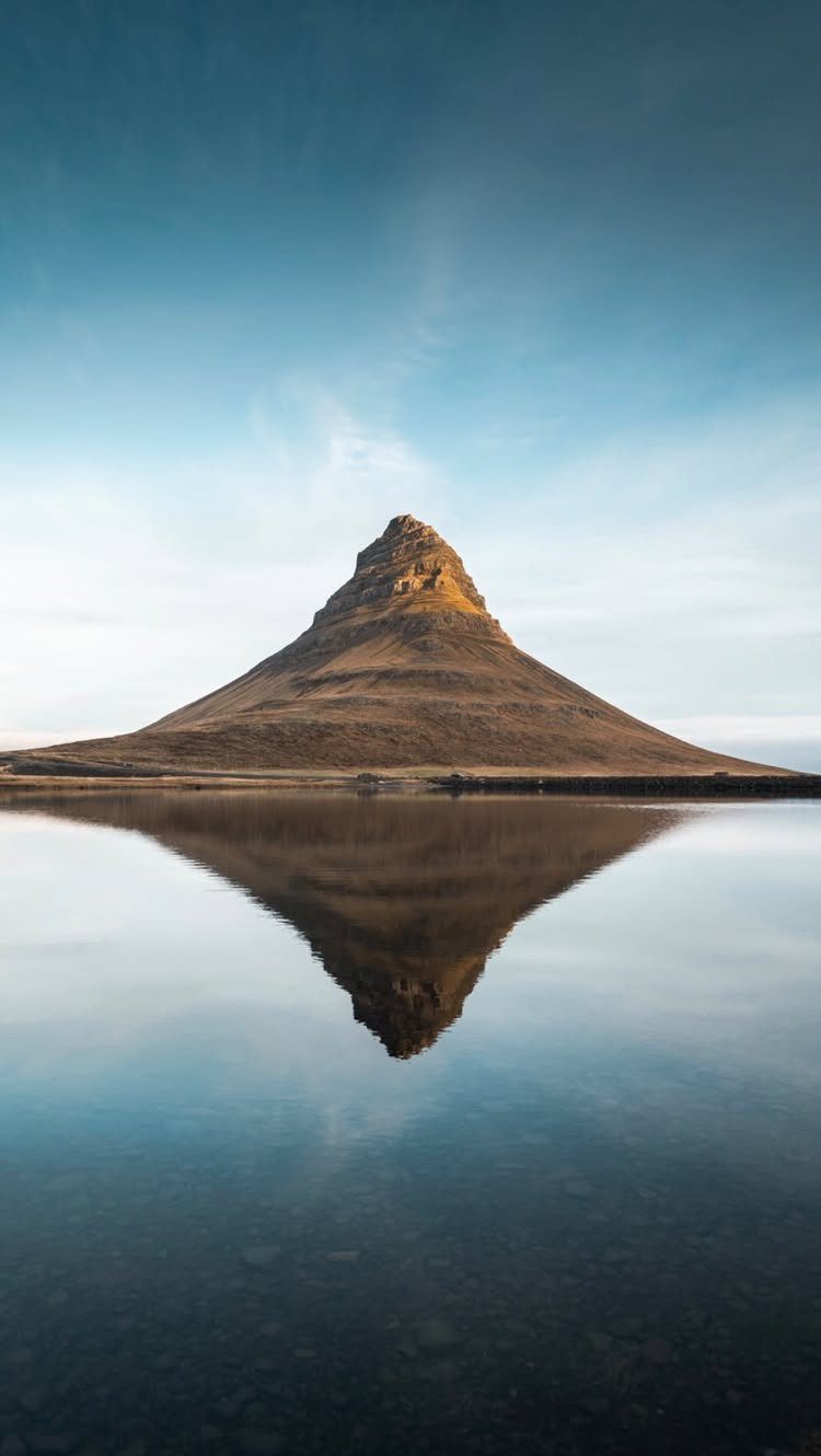 Pointed brown mountain peak reflecting in a still blue lake under clear sky