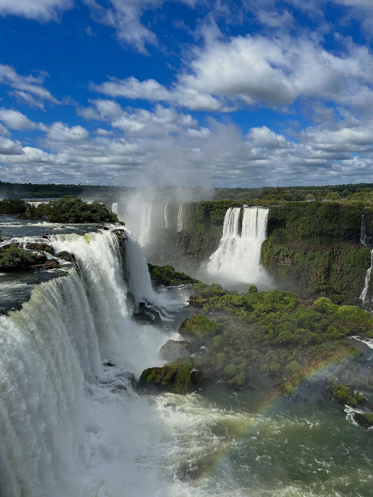 Massive waterfalls cascading over cliffs into a river with a rainbow in the mist.