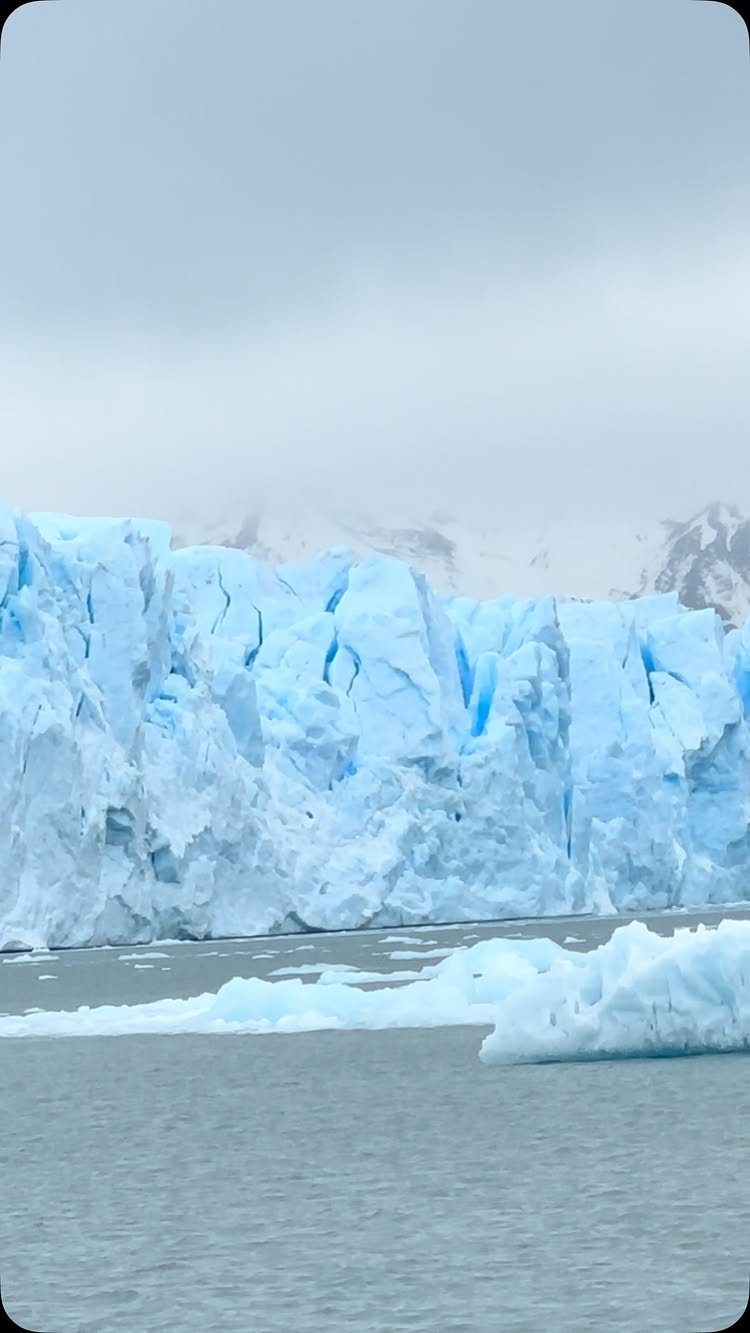 Massive blue glacier wall with ice chunks floating in calm grey water