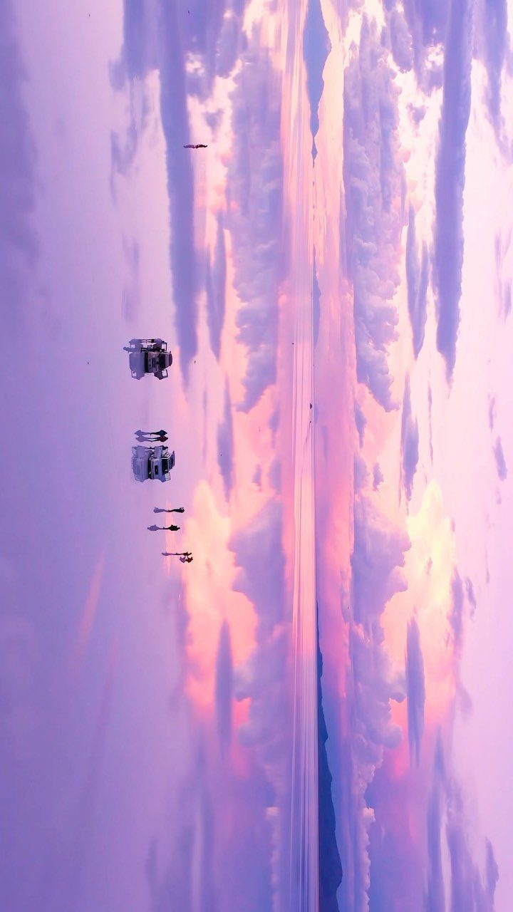Reflective salt flat mirroring a purple and pink sunset sky with distant vehicles.