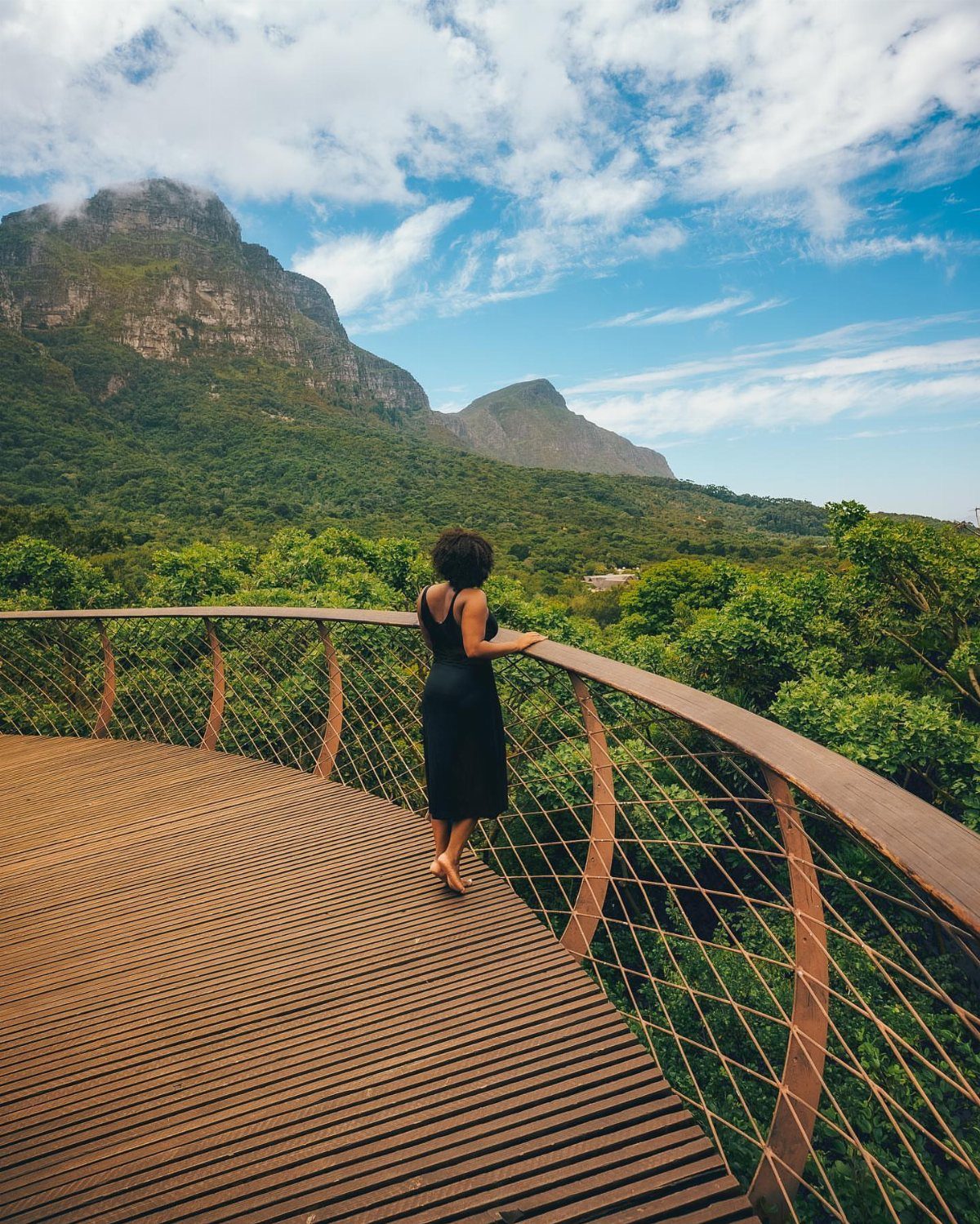 Woman on a wooden boardwalk overlooking a lush green mountain and valley