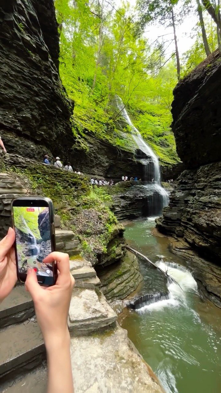 Waterfall cascading down a rocky gorge, captured on a smartphone screen by a visitor.