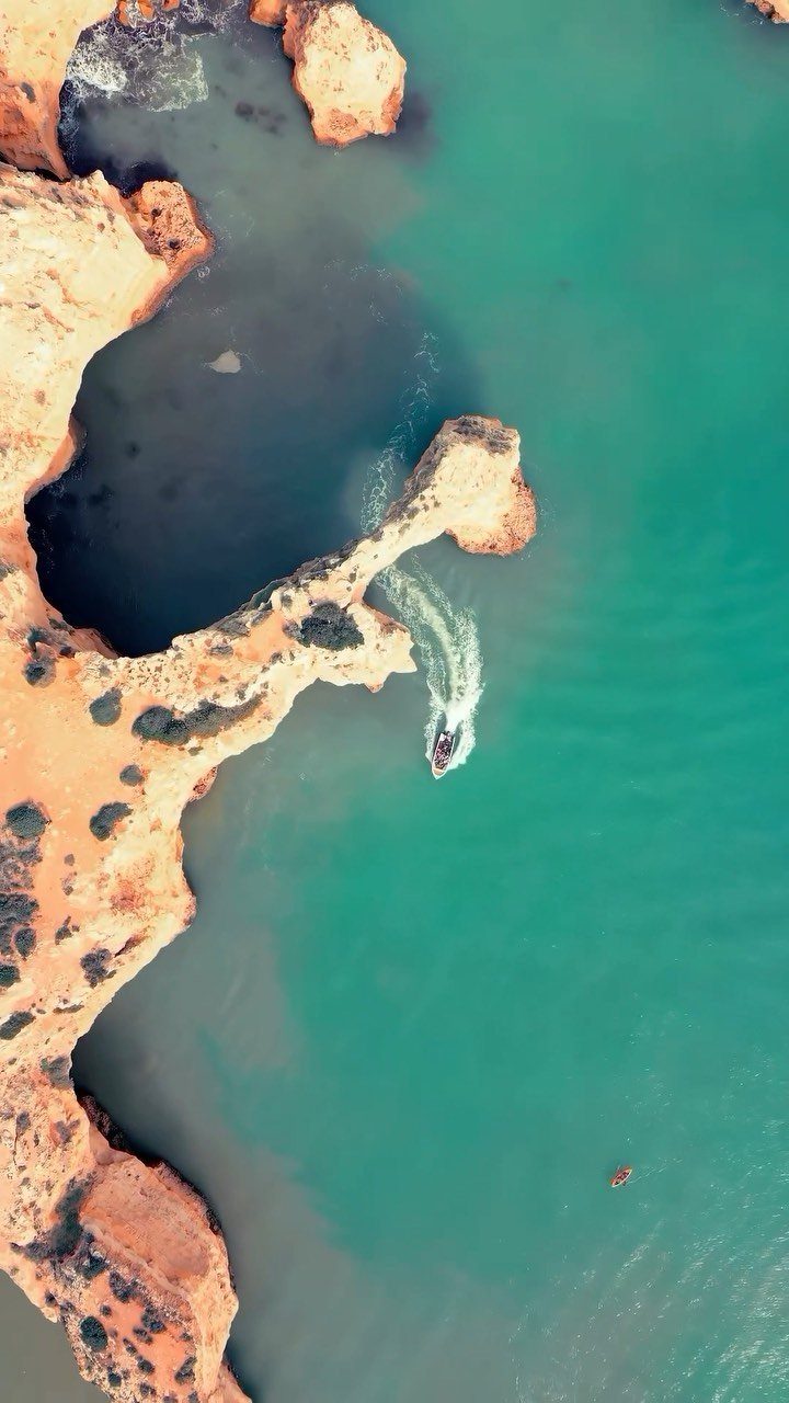 28 Beautiful Places to Travel Around the World 12 Turquoise ocean water surrounding orange rocky cliffs with a small motorboat leaving a wake.