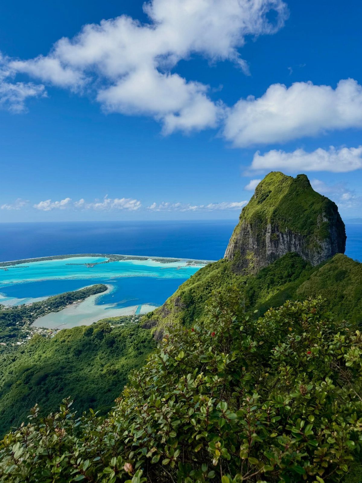 28 Beautiful Places to Travel Around the World 20 Lush green mountain peak overlooking a turquoise lagoon and deep blue ocean.
