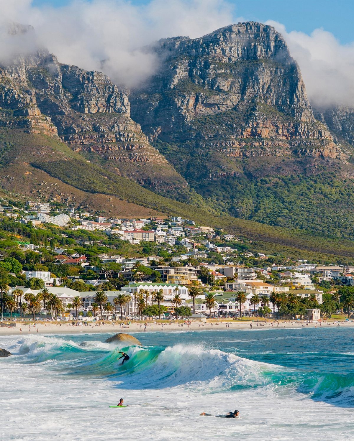 28 Beautiful Places to Travel Around the World 23 Coastal town and surfers at the base of a large flat-topped mountain