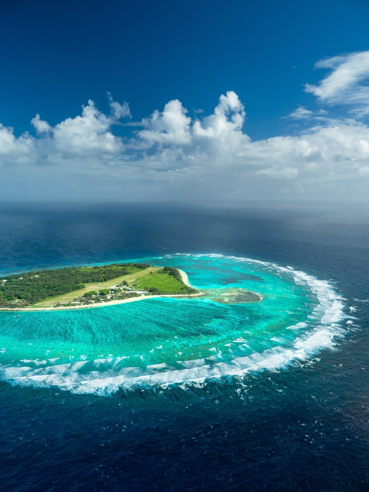 28 Beautiful Places to Travel Around the World 9 Tropical island surrounded by a turquoise coral reef in a deep blue ocean
