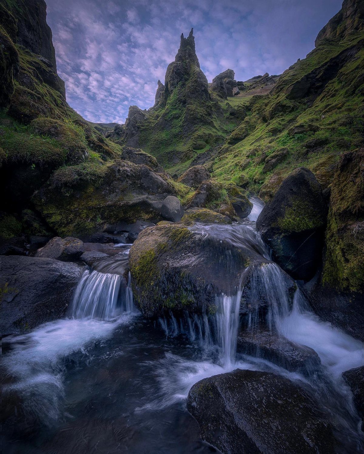 28 Beautiful Places to Travel Around the World 16 Small waterfall flowing over dark rocks between steep, green, jagged volcanic cliffs.