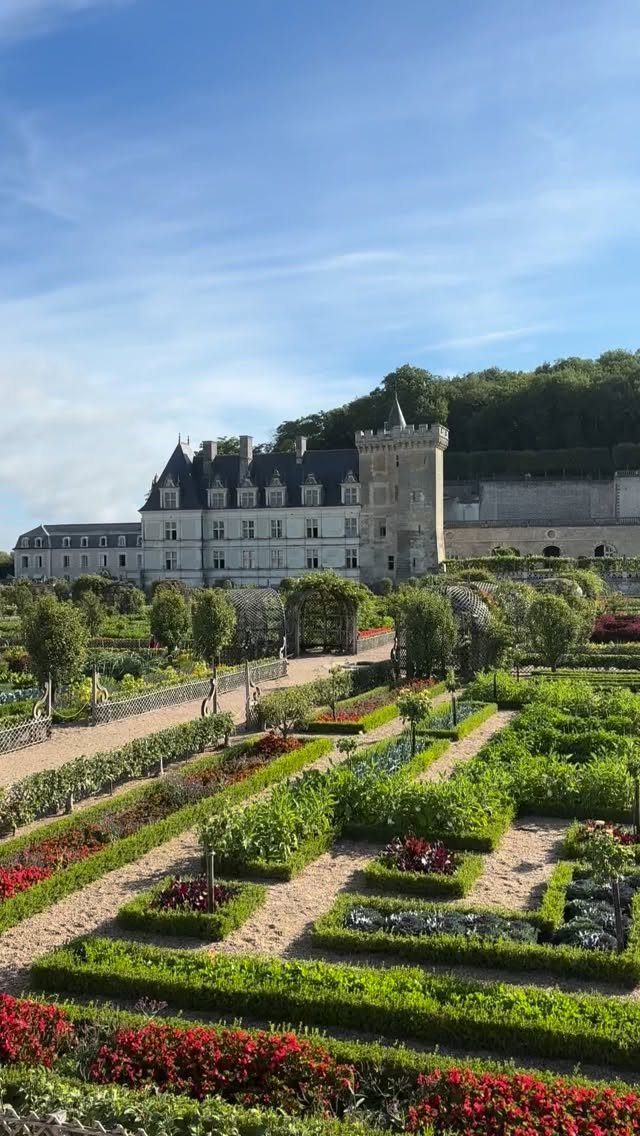 28 Beautiful Places to Travel Around the World 3 White stone château with a tower overlooking a formal geometric garden with red flowers.