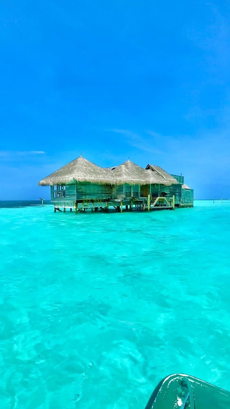 28 Beautiful Places to Travel Around the World 4 Wooden overwater bungalows with thatched roofs in bright turquoise tropical ocean water.