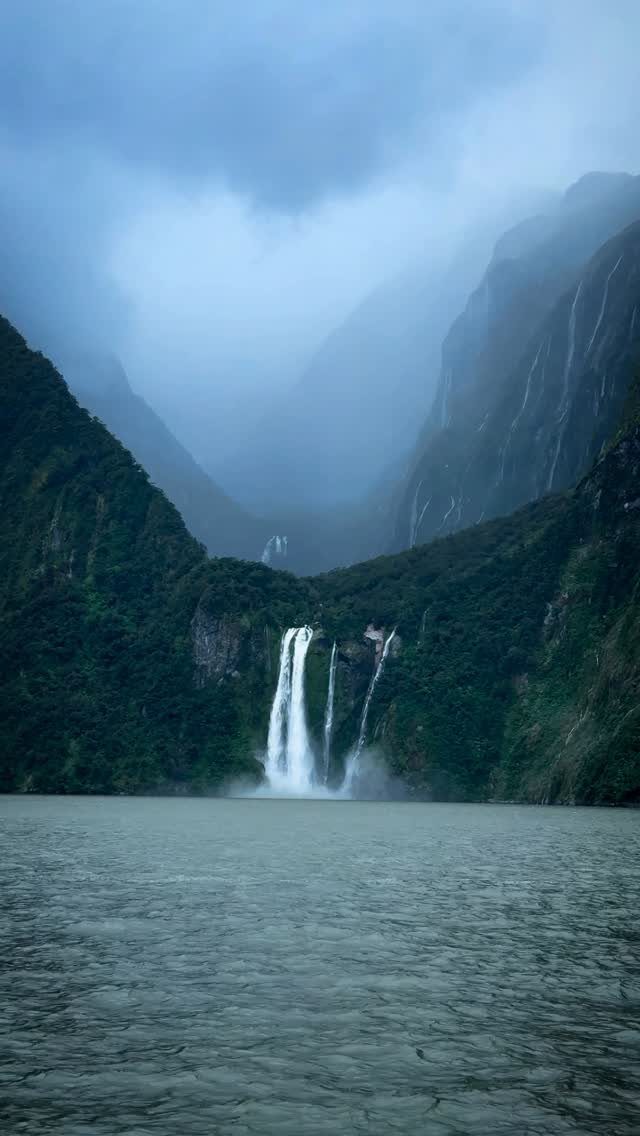 28 Beautiful Places to Travel Around the World 13 Waterfall cascading down green cliffs into a fjord under a misty sky
