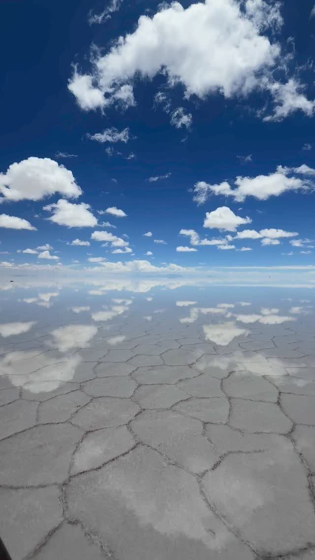 28 Beautiful Places to Travel Around the World 21 White salt flat with hexagonal patterns reflecting a blue sky and white clouds.