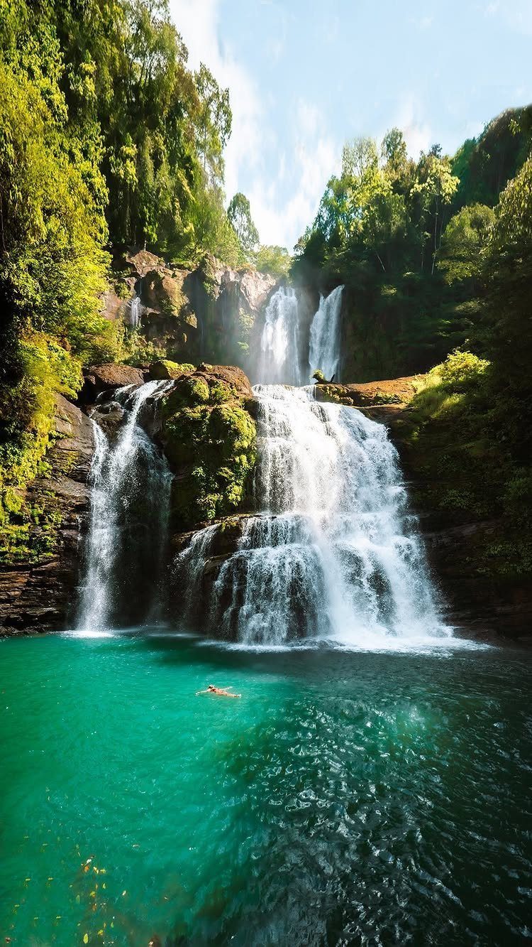 28 Beautiful Places to Travel Around the World 28 Multi-tiered waterfall cascading into a turquoise pool surrounded by lush green tropical forest.