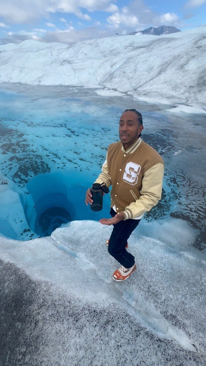 Bucket List Travel Destinations in the USA: 33 Ideas 26 Man in varsity jacket standing on a glacier next to a deep blue ice hole.