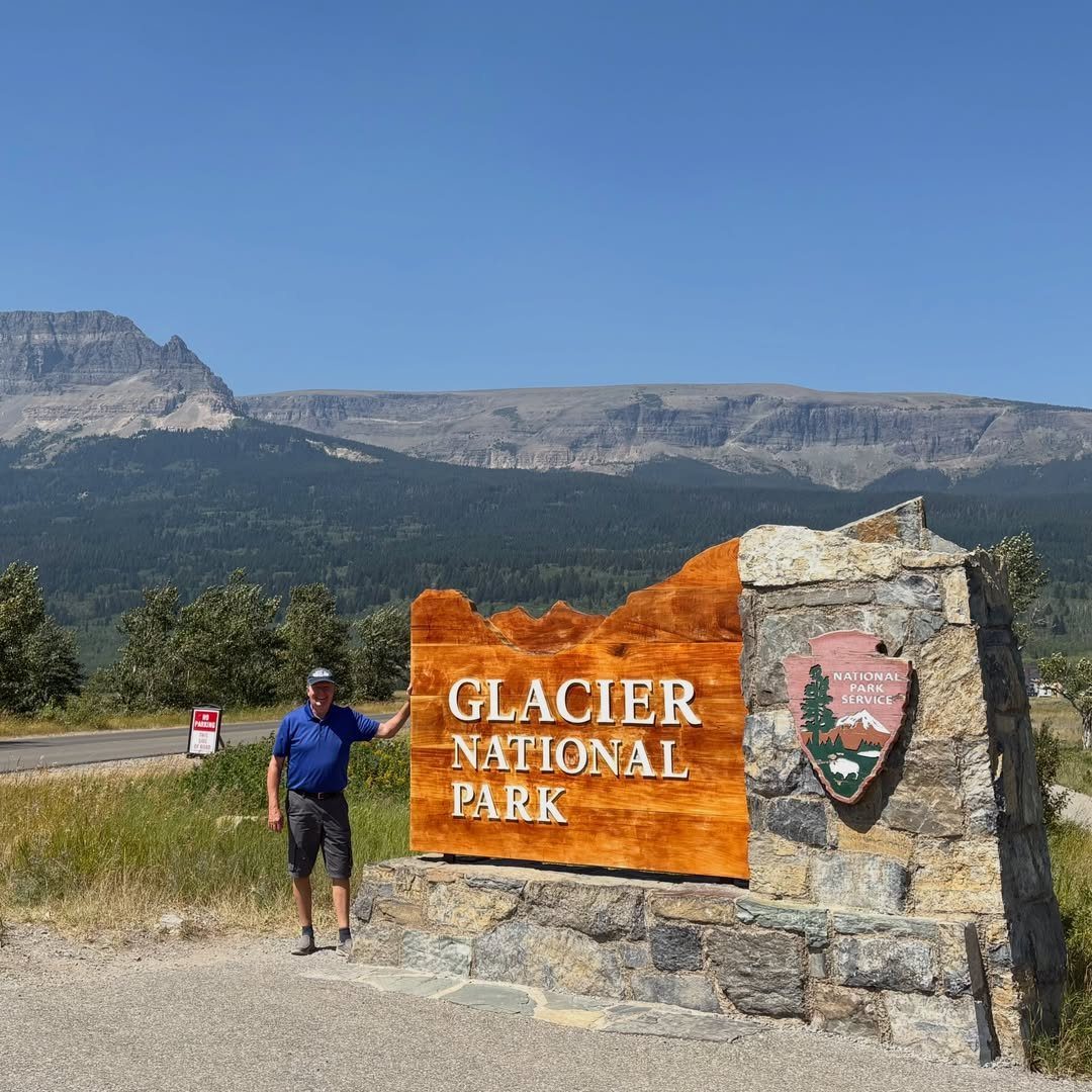 Bucket List Travel Destinations in the USA: 33 Ideas 8 Man standing by the Glacier National Park entrance sign with mountains in background