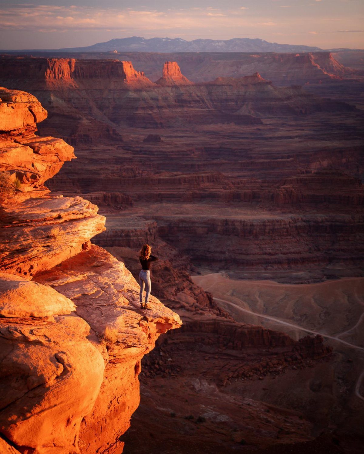 Bucket List Travel Destinations in the USA: 33 Ideas 1 Person standing on a red rock cliff overlooking a vast desert canyon landscape.