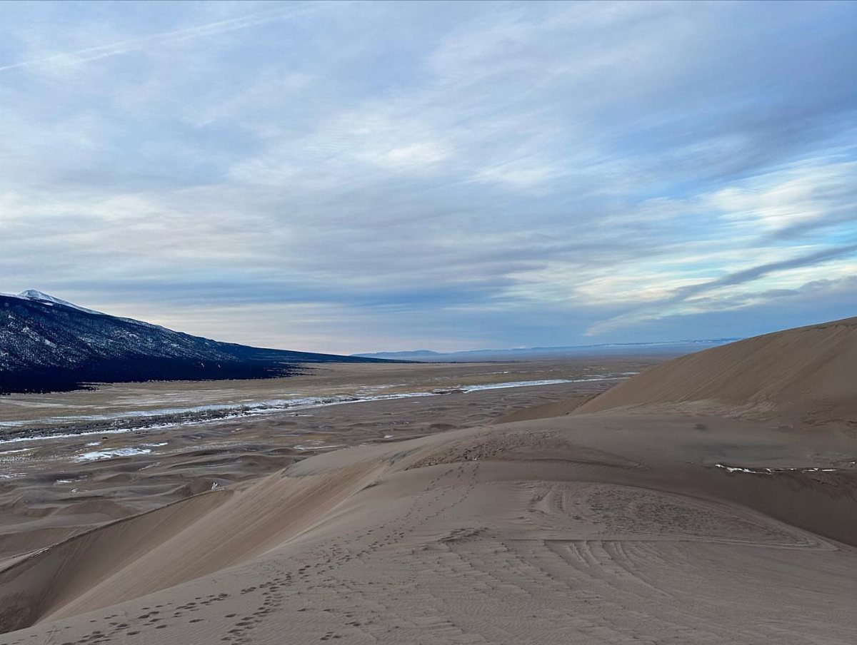 Bucket List Travel Destinations in the USA: 33 Ideas 10 Large tan sand dunes overlooking a valley and distant snow-capped mountains.
