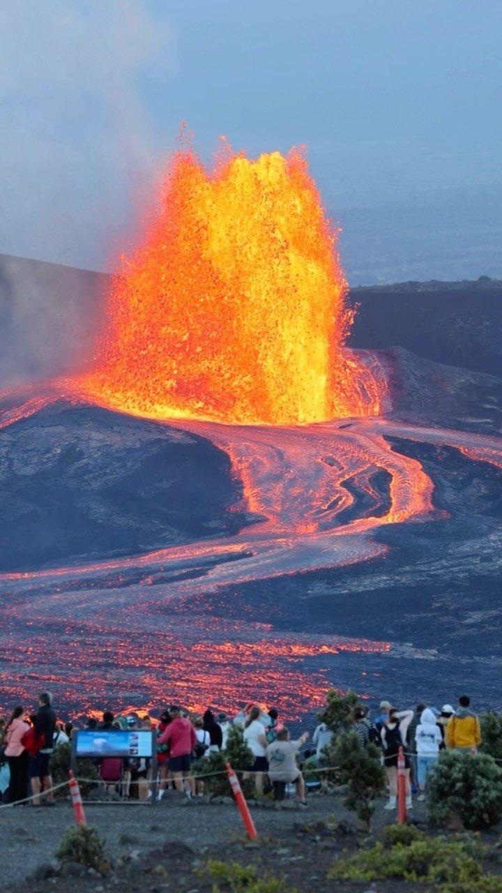 Bucket List Travel Destinations in the USA: 33 Ideas 27 Bright orange lava erupting from a volcano with onlookers watching from a distance.