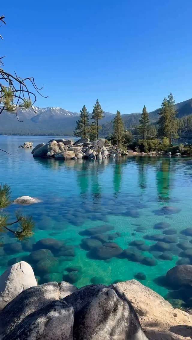 Bucket List Travel Destinations in the USA: 33 Ideas 5 Turquoise alpine lake with clear water, grey boulders, and distant snow-capped mountains.