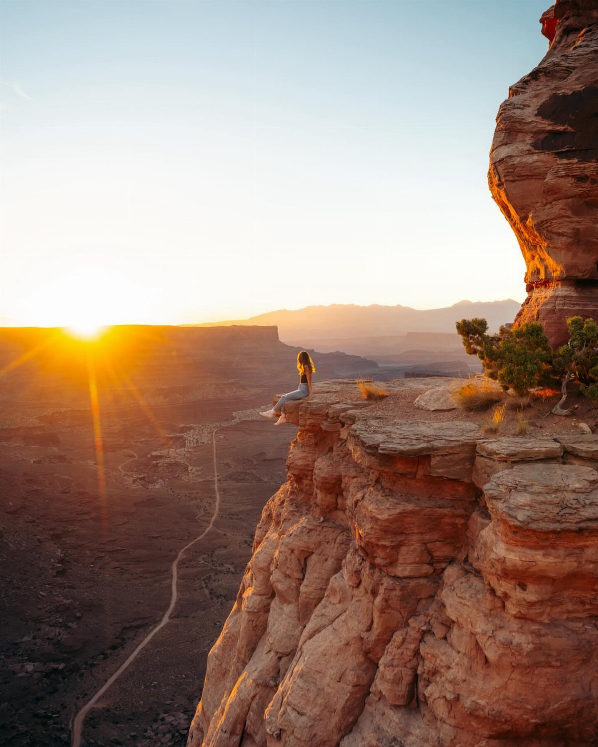 Bucket List Travel Destinations in the USA: 33 Ideas 13 Woman sitting on a red rock cliff overlooking a desert canyon at sunset
