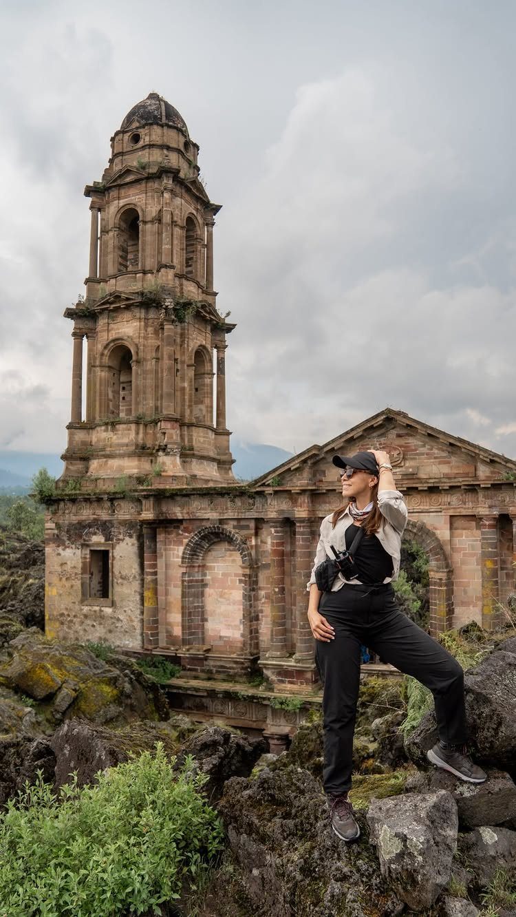 16 Cheap Pretty Places to Travel on a Tight Budget 4 Woman standing on volcanic rocks in front of ancient stone church ruins.