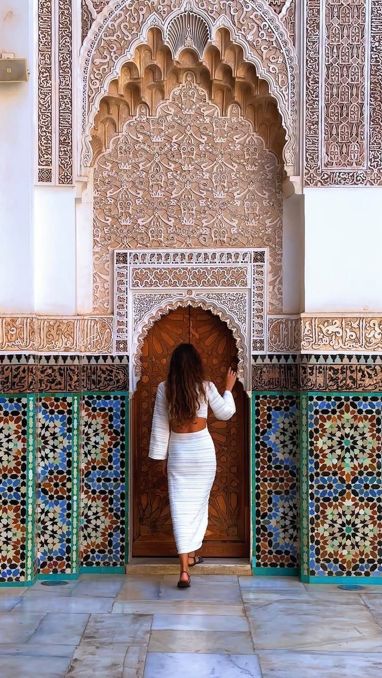 16 Cheap Pretty Places to Travel on a Tight Budget 1 Woman in white dress standing before an ornate carved door with colorful Moroccan tiles.