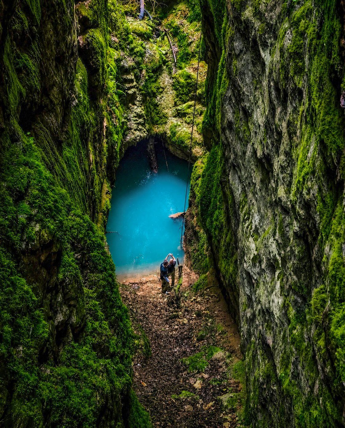 16 Cheap Pretty Places to Travel on a Tight Budget 14 Person standing in a mossy green canyon overlooking a turquoise blue pool